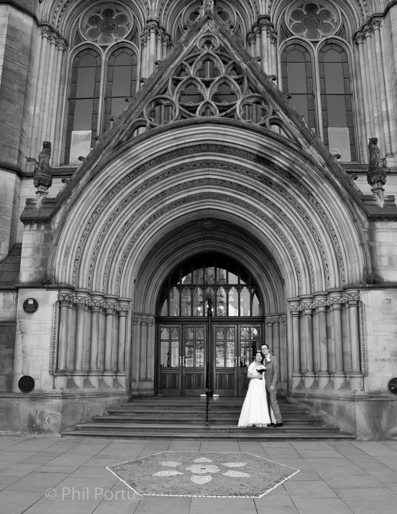 A black and white image shows a couple standing on steps in front of an ornate stone building.