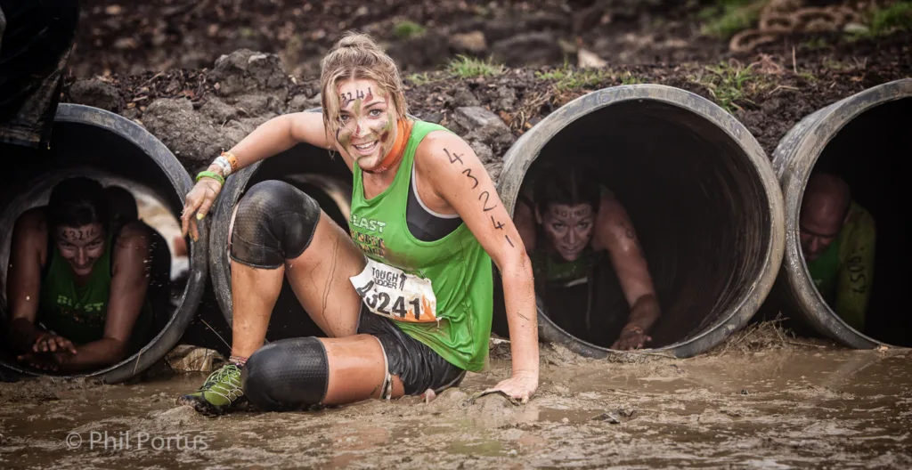 A woman covered in mud sits between large concrete pipes with other people visible inside.
