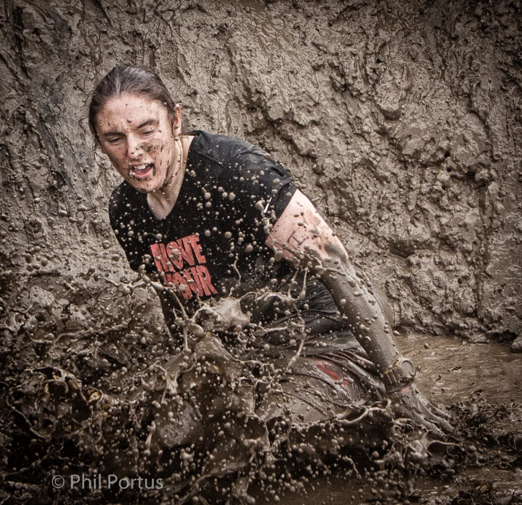A person wearing a dark t-shirt crawls through muddy water, creating a splash.