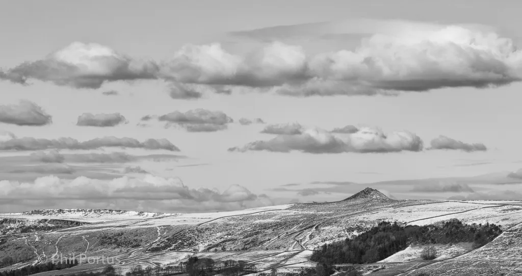 A black and white landscape shows rolling hills with scattered snow and a dramatic cloudy sky.