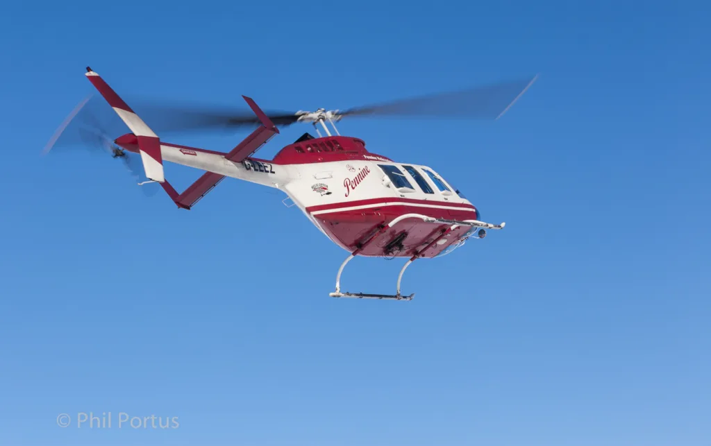 A red and white helicopter flies against a clear blue sky with its rotors spinning.