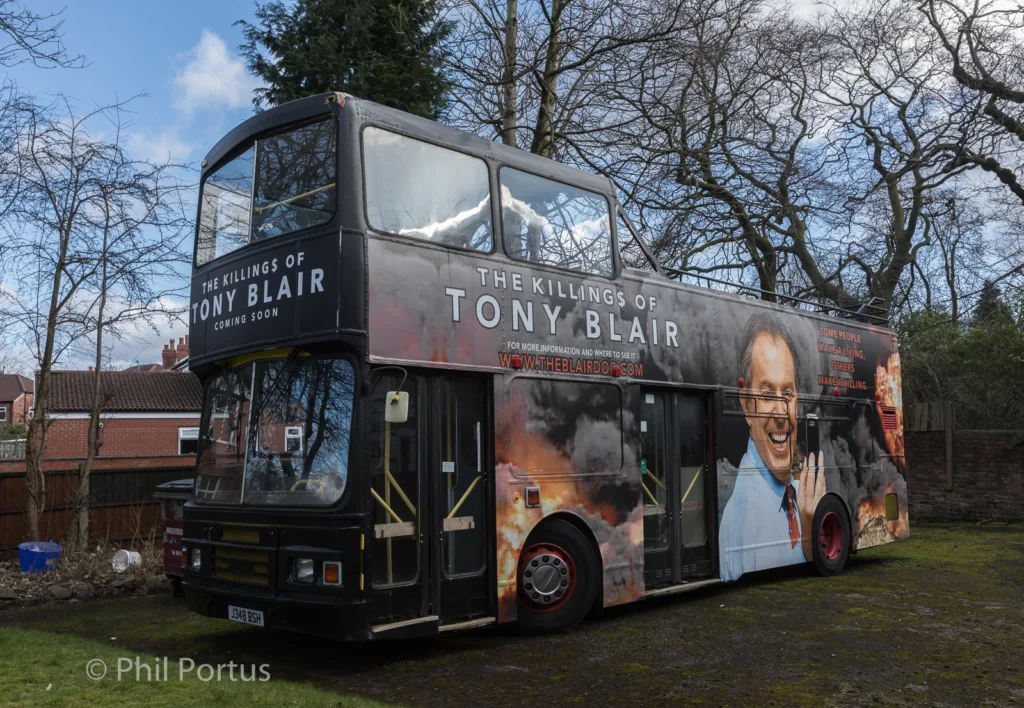 A double-decker bus is parked on a residential street with advertising posters covering its exterior.