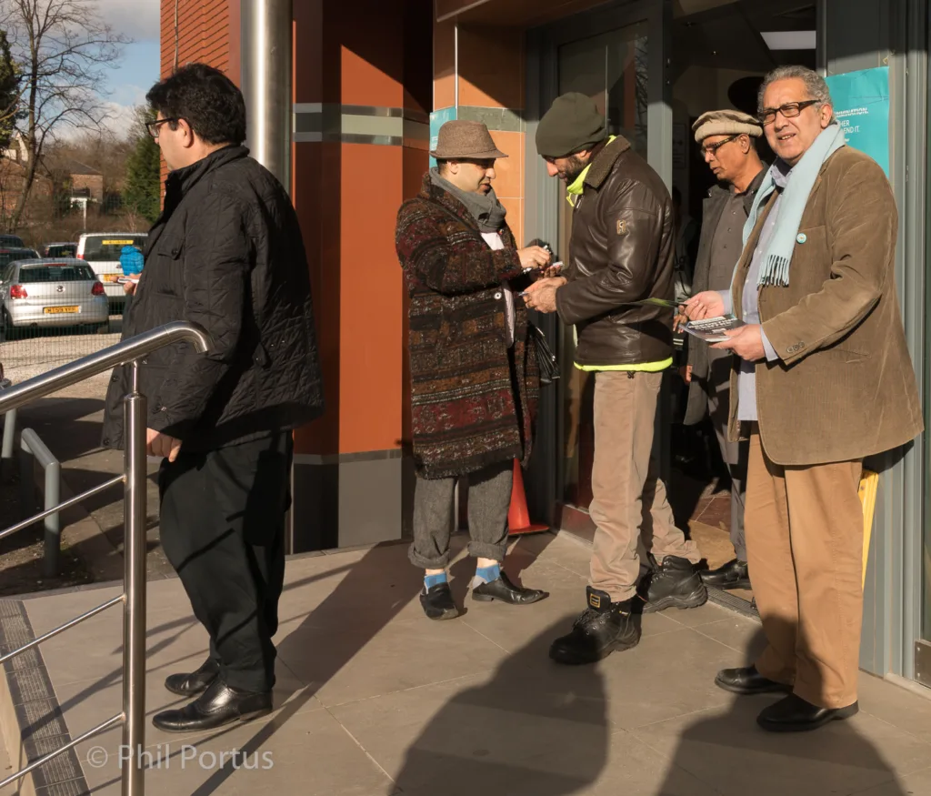 Four people stand on a paved area in sunlight, some wearing hats and coats.