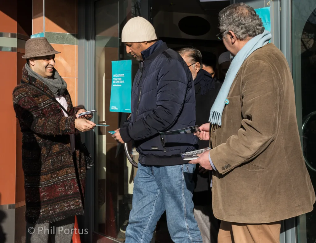 Three people stand near a doorway, looking at something in their hands.