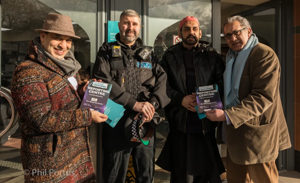 Four people stand near a doorway holding flyers, dressed in warm clothing.