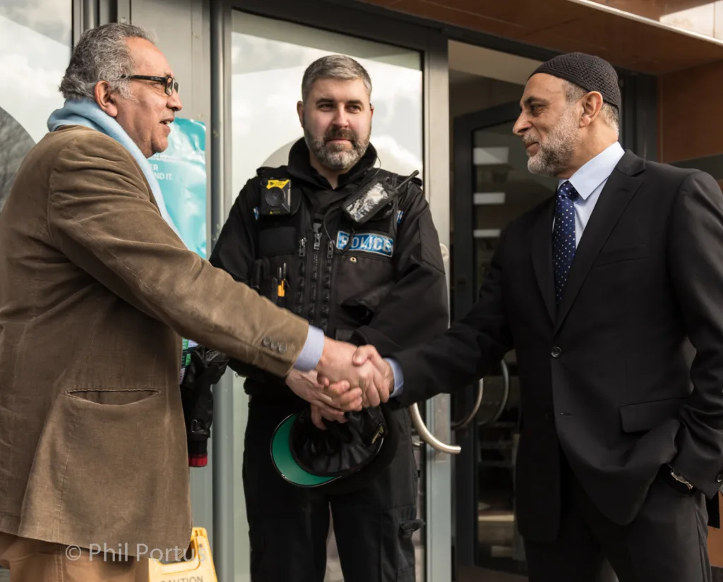 Three men shake hands outside a building; one wears a police uniform.