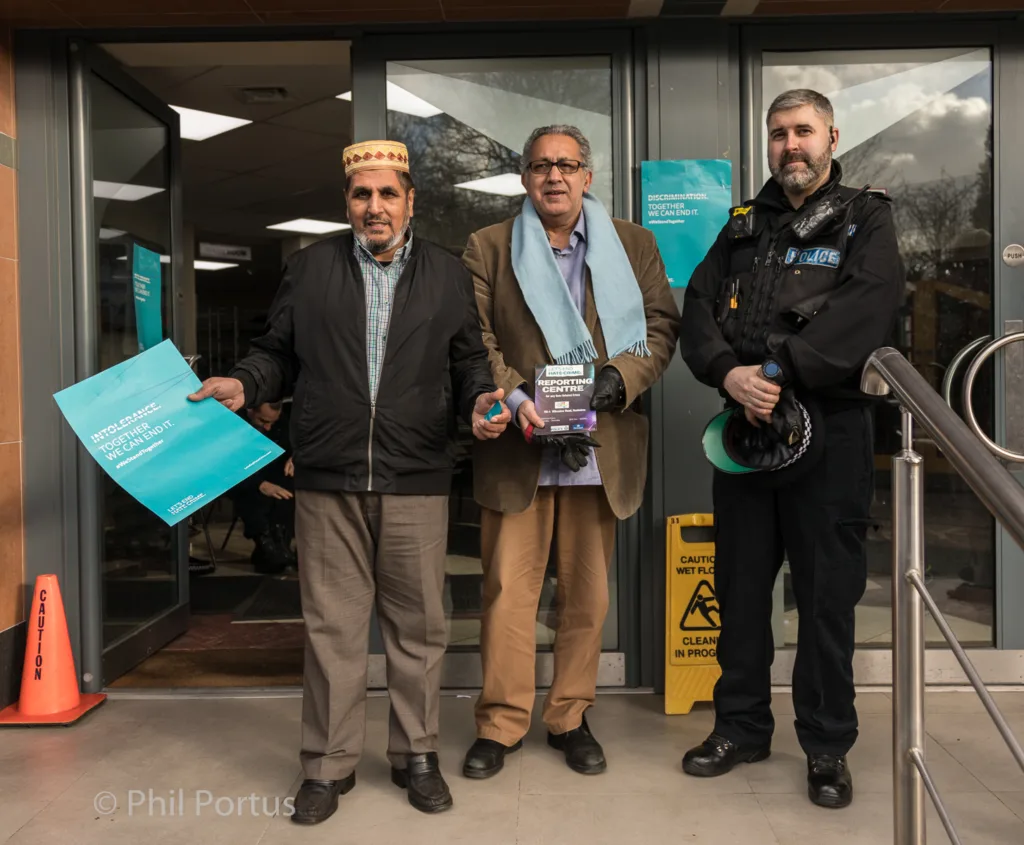 Three people stand outside a building entrance; one wears a police uniform.