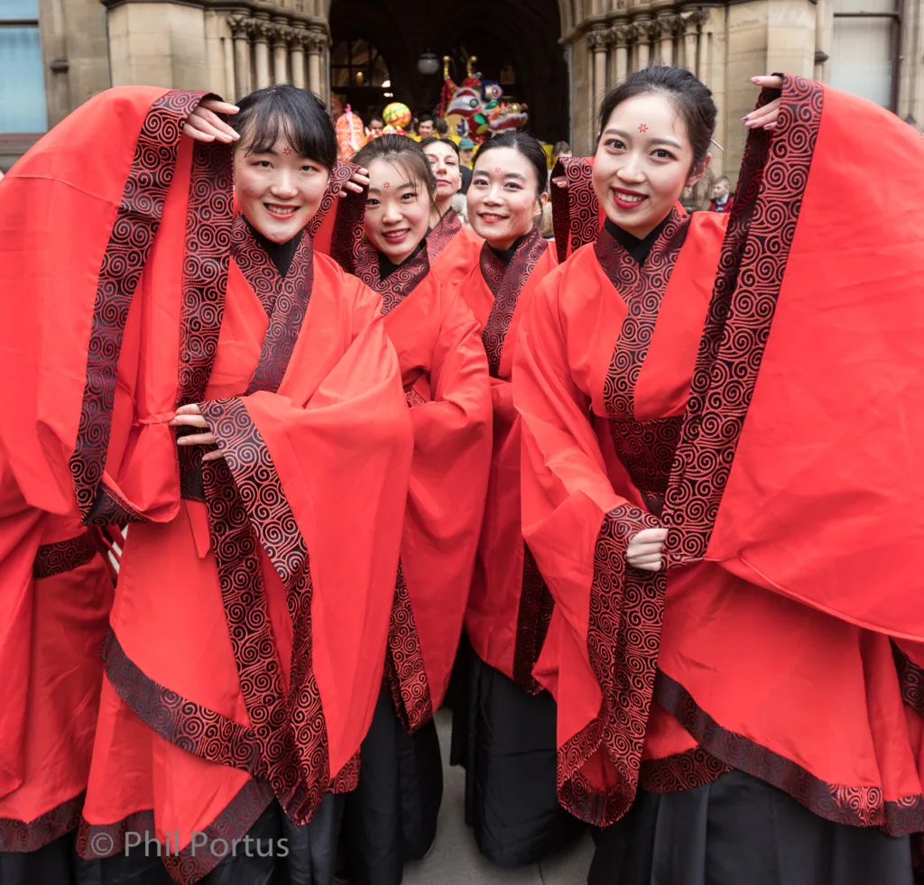 A group of people wearing red and dark patterned garments smile closely together.