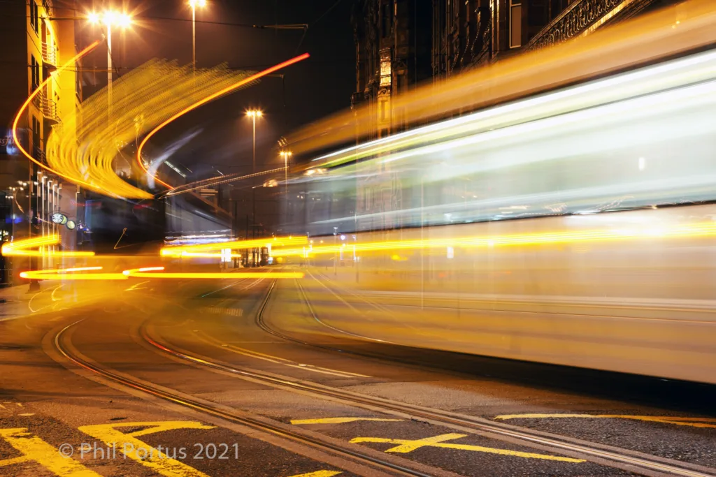 Streaks of yellow light from a vehicle moving quickly across a paved road at night.