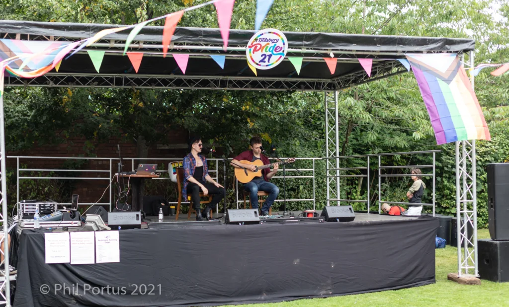 Three people perform on a stage decorated with colorful flags and bunting.