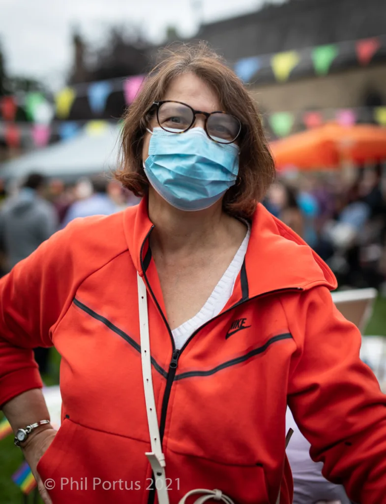 A person with glasses and a face mask wears an orange jacket at an outdoor event.