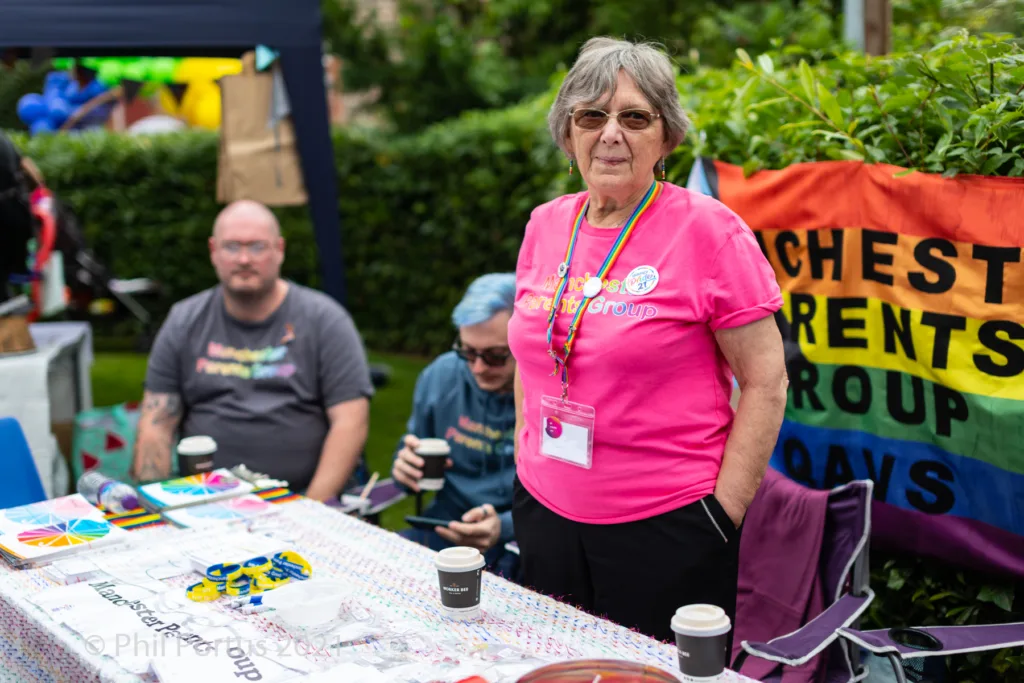 Three people stand behind a table covered with colorful papers at an outdoor event.