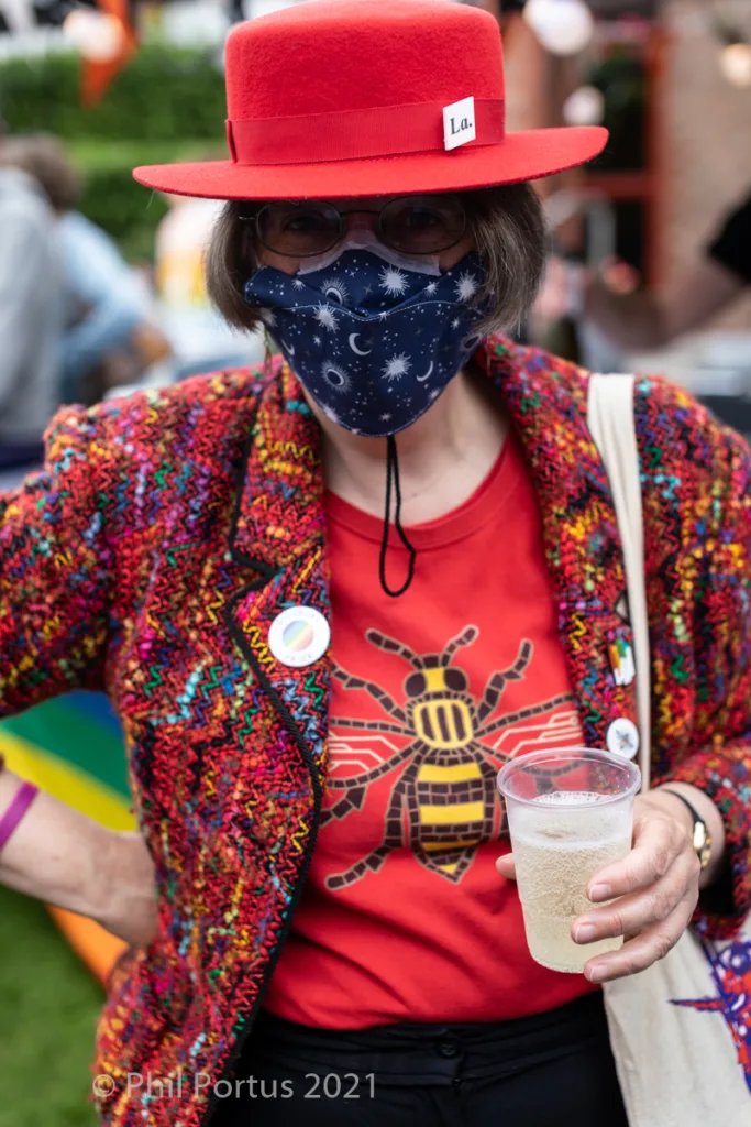 A person wearing a red hat, patterned mask, and colorful jacket holds a drink in a clear plastic cup.