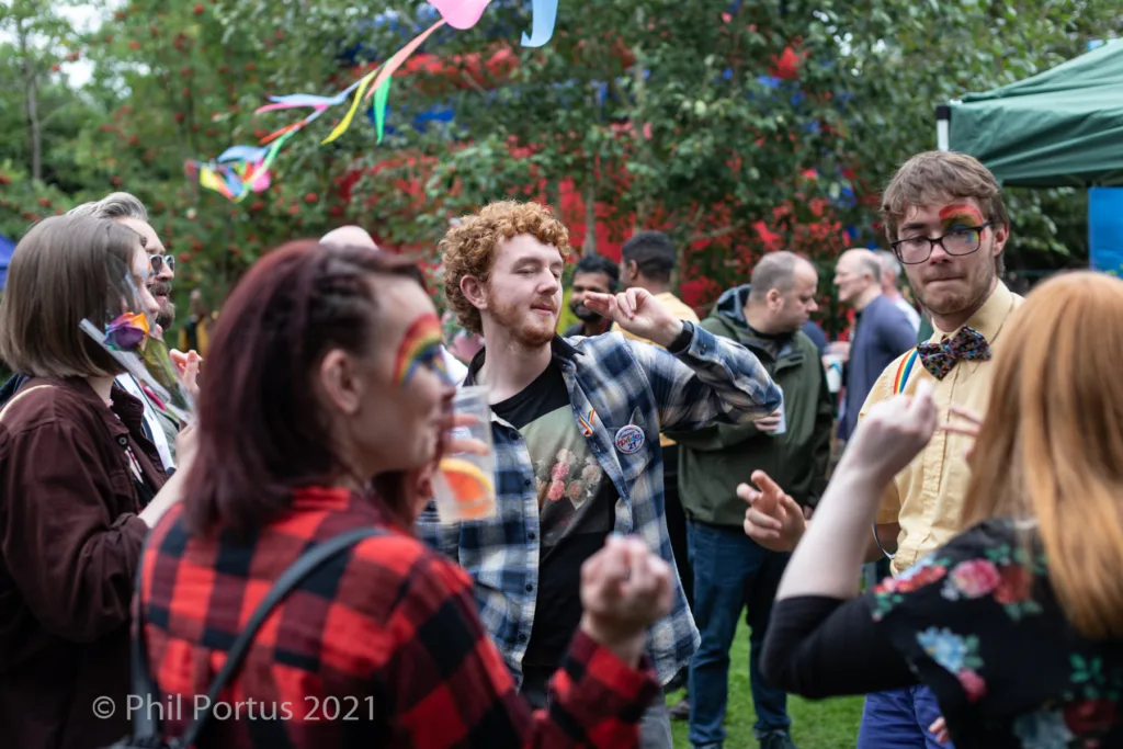 People dance outdoors at an event with colorful flags strung between trees.