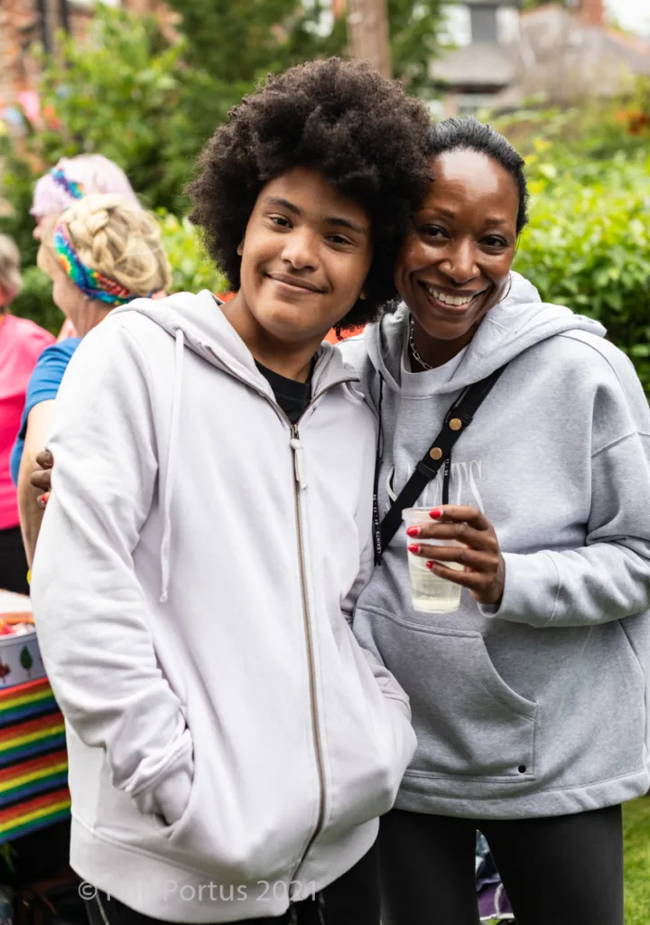 Two people with smiles stand close together in a casual outdoor setting.