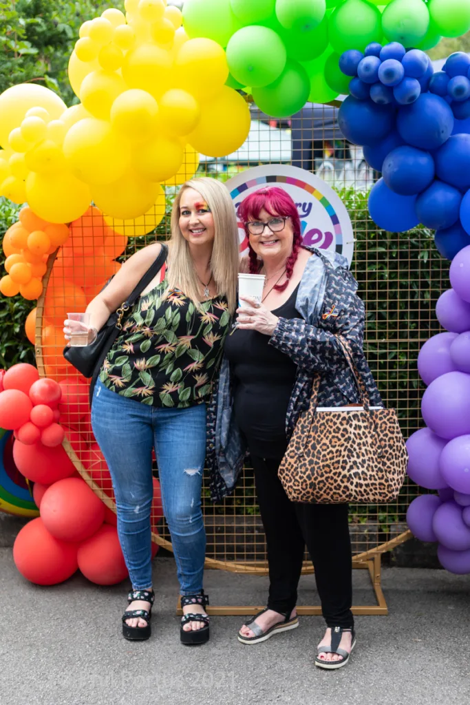 Two people smile for a picture in front of a colorful balloon arch.