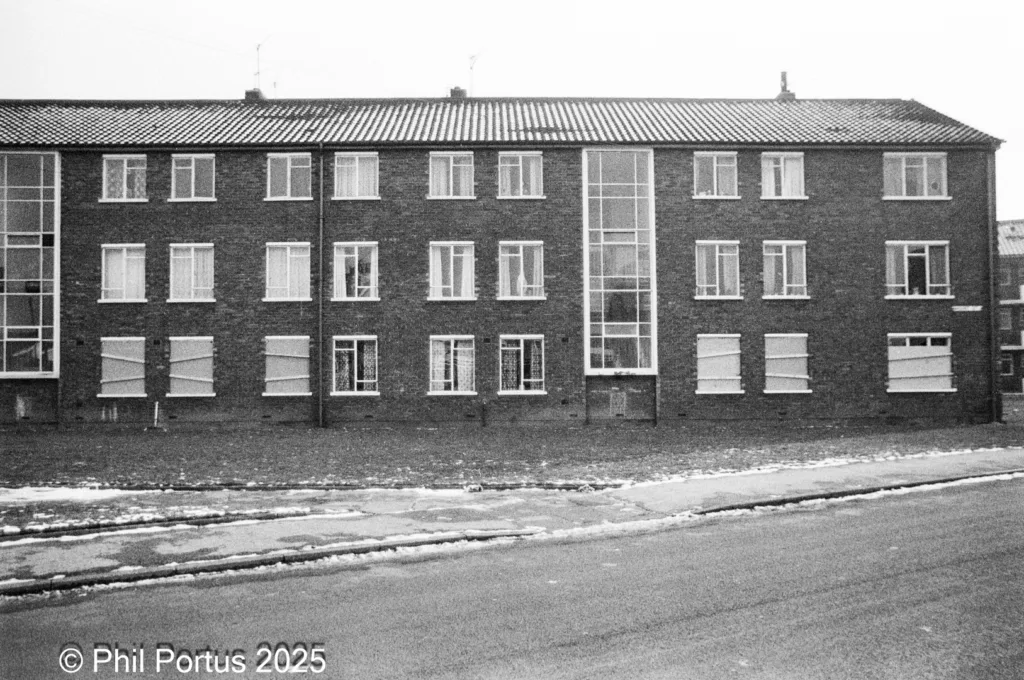 A long, rectangular brick building with many windows is visible against a grey sky.